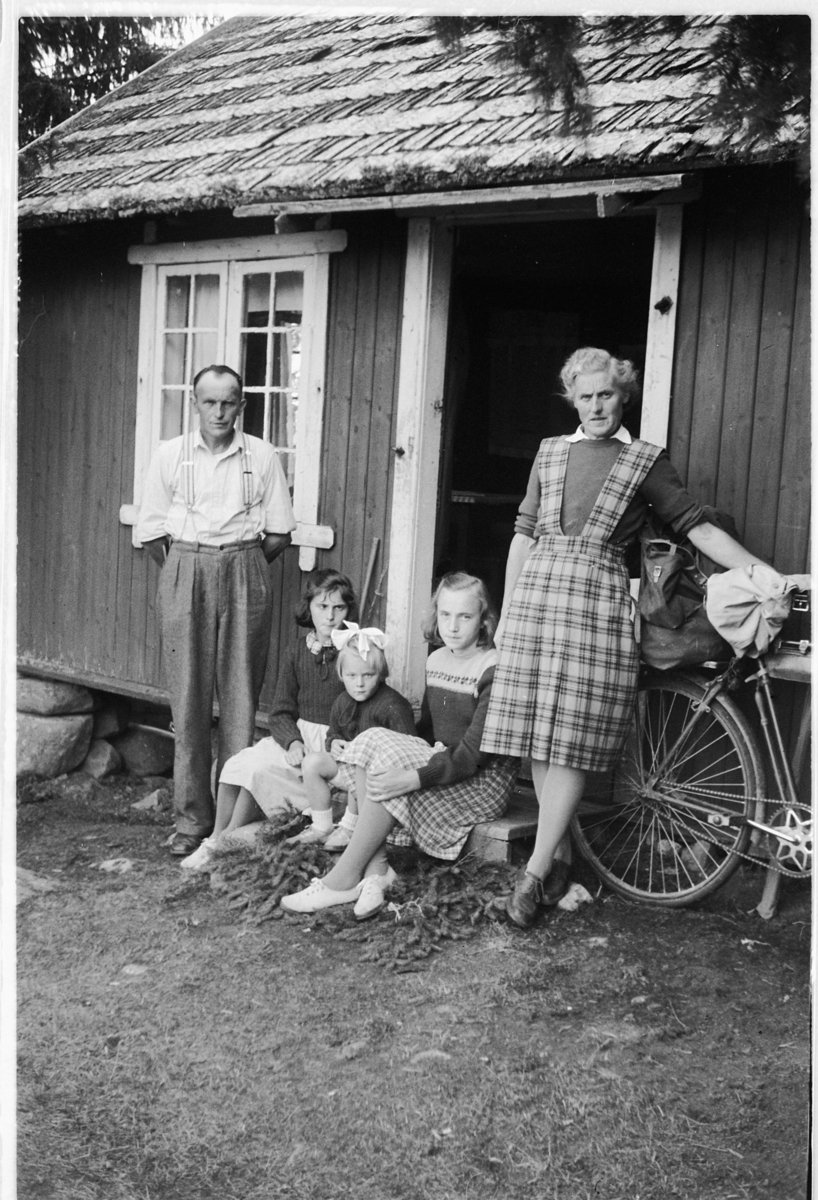 Håkon Prestkværn, Ukjent mann, kvinne og tre jenter ved inngangsdøra til et hus. Kvinnen holder i en sykkel.