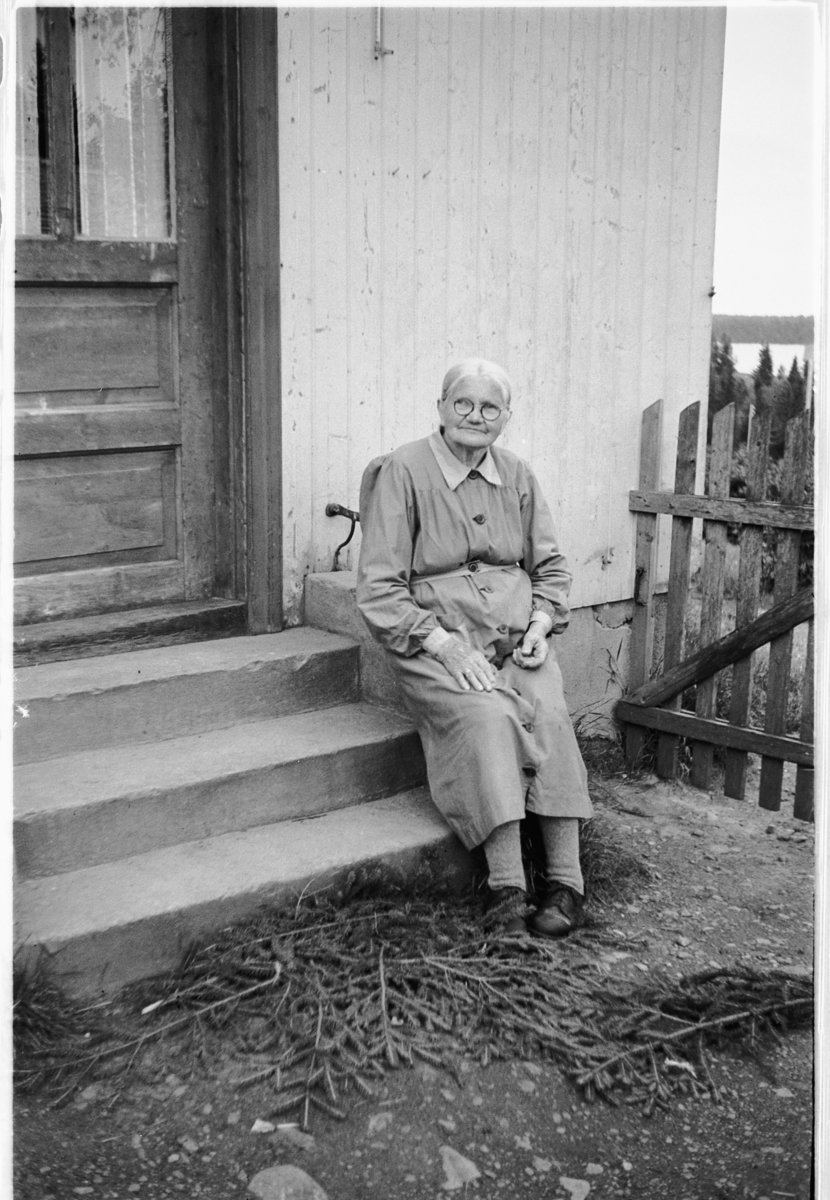 Håkon Prestkværn, Eldre kvinne sitter på trappa til et hus.