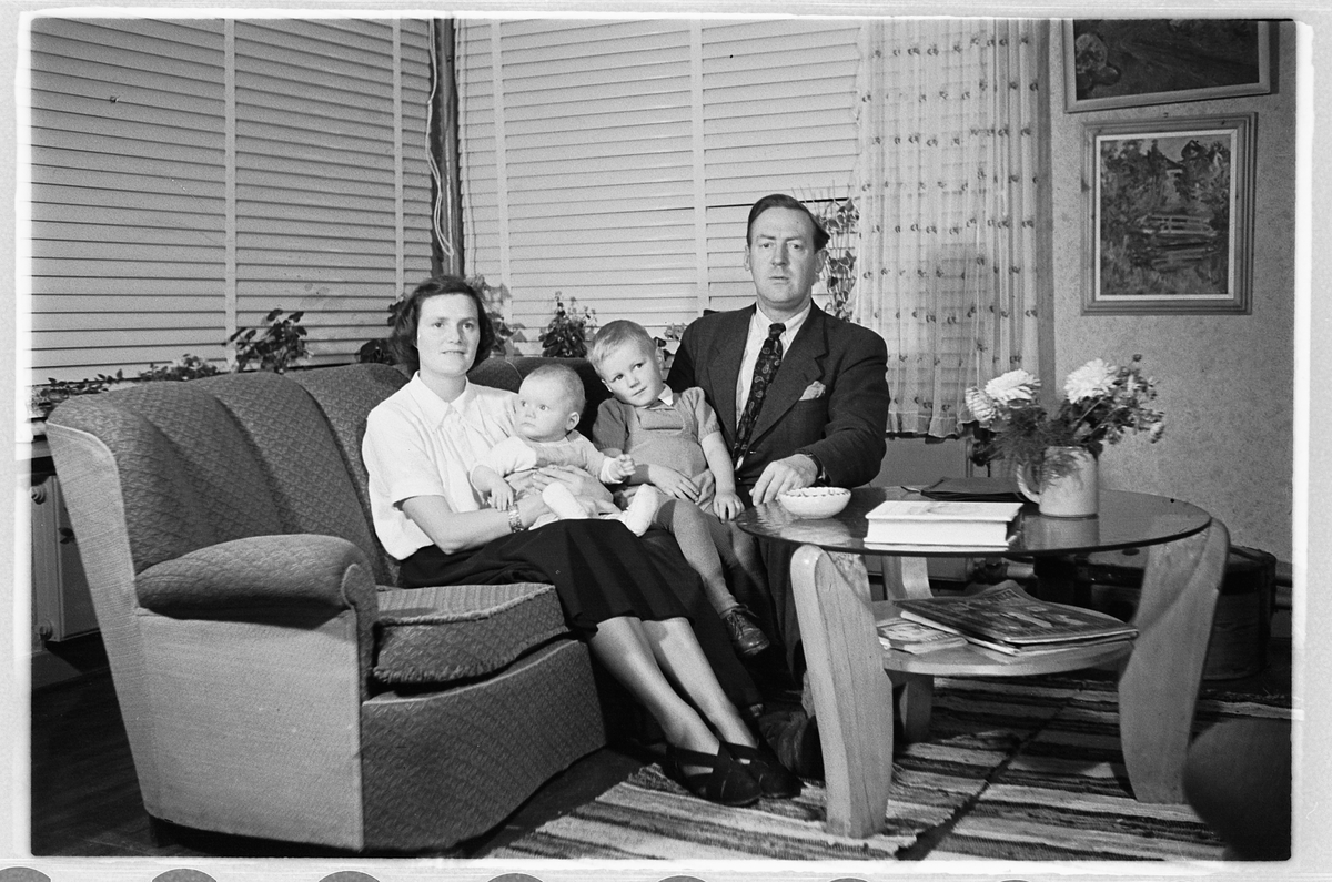 Håkon Prestkværn, Interiør, stue. Kvinne og mann i en sofa med en baby og en gutt.