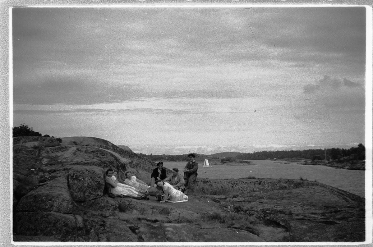 Håkon Prestkværn, Gruppe kvinner og menn sitter på et svaberg i skjærgården.