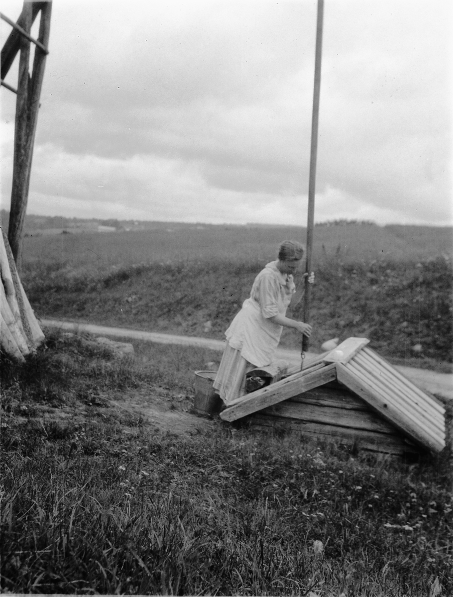 Ragnvald Andersen, Ukjent kvinne henter vann ved en vannpost, brønn.