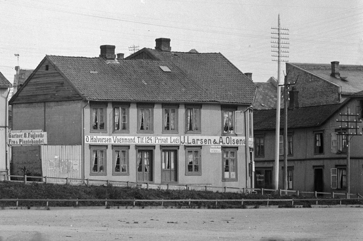 Hans Emil Erichsen, Østre Torg. Bebyggelsen langs Grønnegata i Hamar. Utsnitt. Gartner O. Fuglseth, Vognmand O. Halvorsen, Privat Logi, fotografene J. Larsen & A. Olsen, Fotografisk atelier. Se HHB-08683.