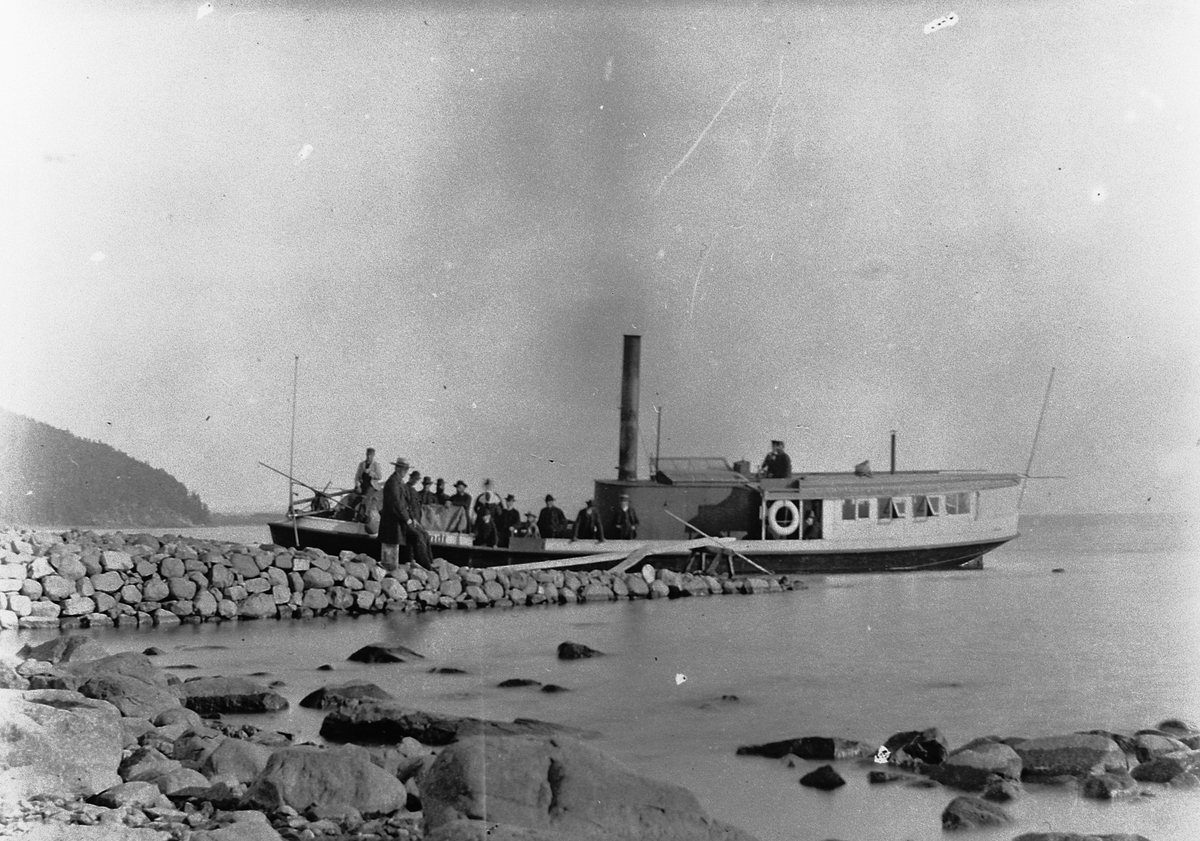 Hans Emil Erichsen, D/S Lettvindt ved Jessnes Brygge i Ringsaker. Kaptein Christian Jensen står i styrhuset. Mjøsbåt. Steinbrygge. Lettvindt var Mjøsas første propellbåt, bygd i 1867. Senere ble den ombygd og døpt Helgøy. Den endte sine dager ved Minnesund i 1960 under navnet Mira.