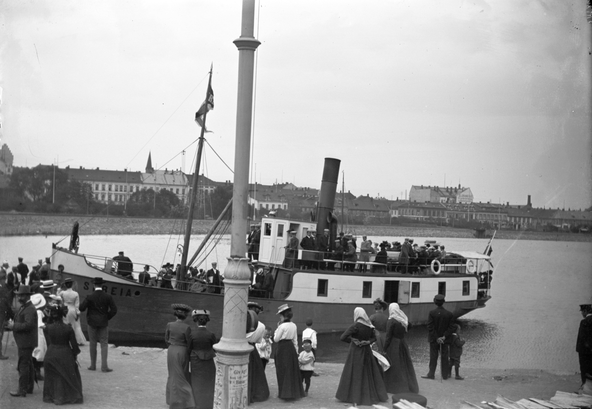 Johannes Larsen Alhaug, D/S Skreia ved Hamar brygge. Mennesker venter på av og påstigning. Båten ble bygget for "Hamar dampskibsselskap" i 1902 og hugget opp i 1957.
