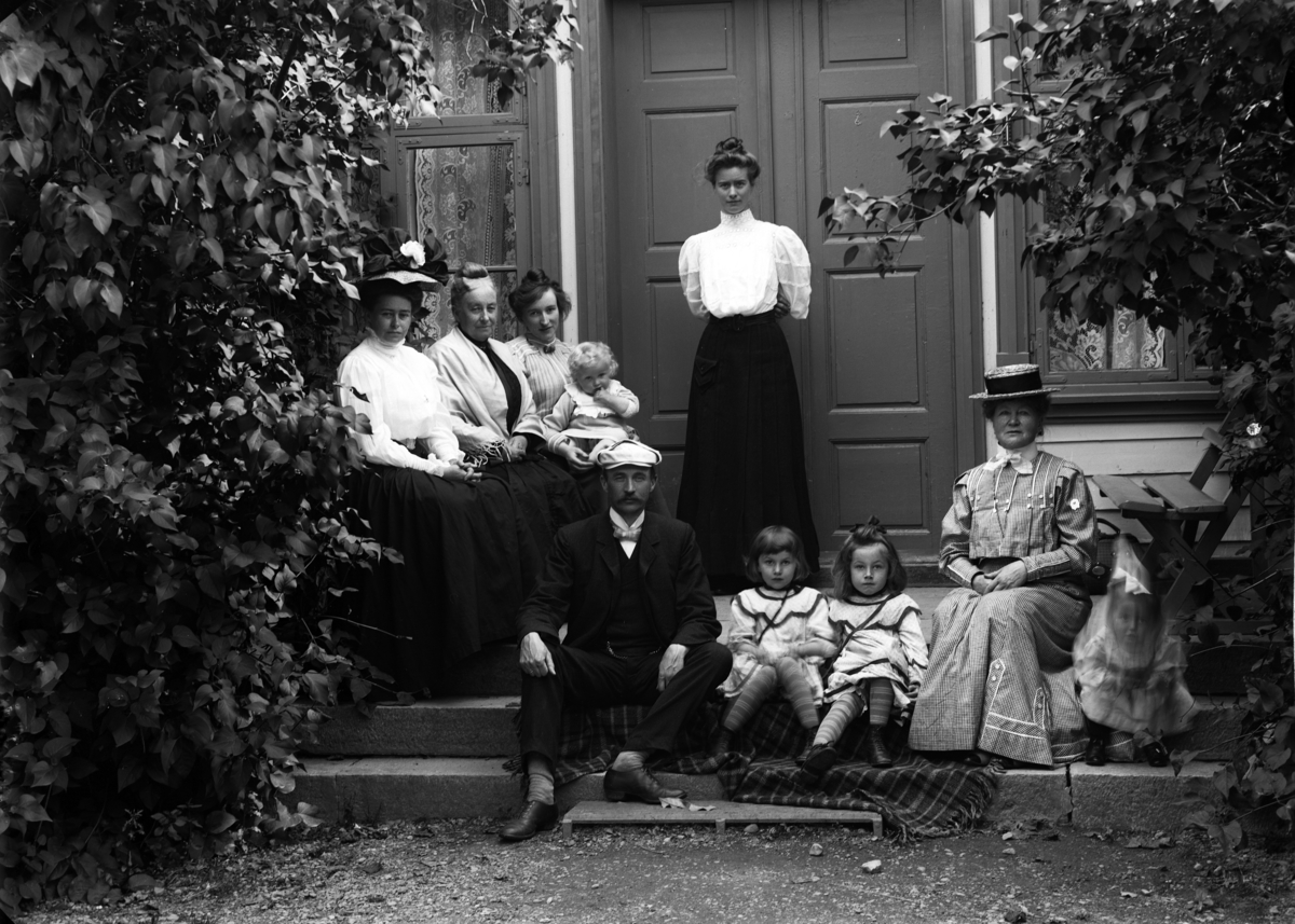 Martin Finborud, Familiegruppe, Mellbye, Grefsheim. Johan Egeberg Mellbye (1866-1954) sittende på trappa, og hans kone Emilie stående bakerst.