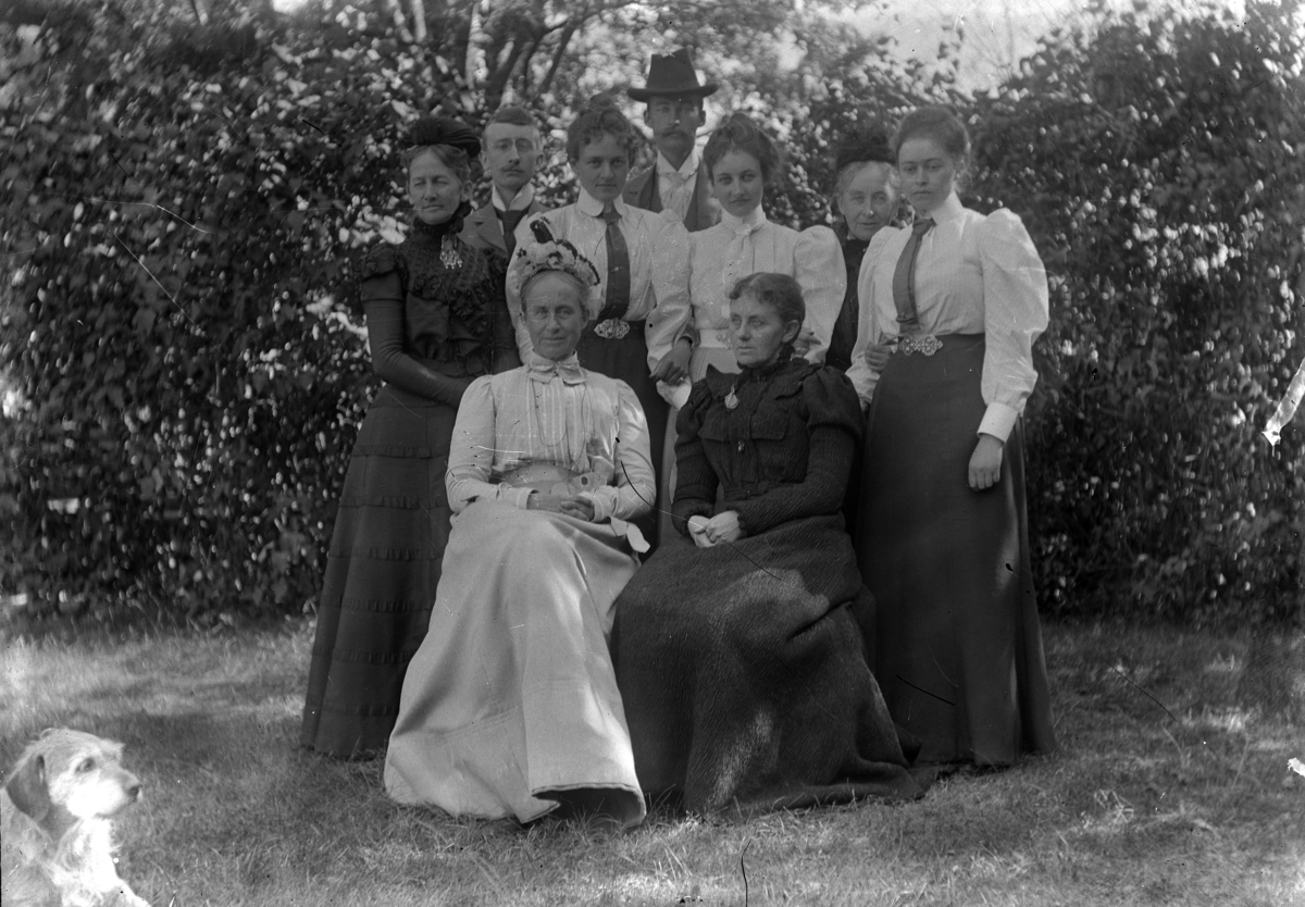 Martin Finborud, NI MENNESKER FOTOGRAFERT I HAGEN. FV. SITTENDE: JULIE MUNCH GRAM OG LAURA LARSEN NAUR F. MUNCH. FV. STÅENDE: AGNES PETERSSON F. IRGENS, MADS GRAM, HEKLA MUNCH, JANKEN GRAM, LOL MISEN F. MELLBYE, SOFIE MELLBYE F. MUNCH, SOFIE PIHL F. MELLBYE