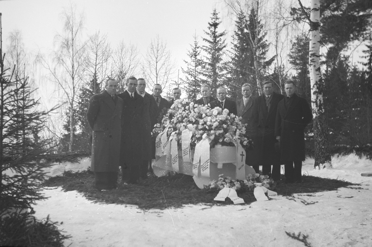 Håkon Prestkværn, Begravelse. Olafsen 1946. Gruppe etterlatte samlet rundt kisten. Blomster, granbar.