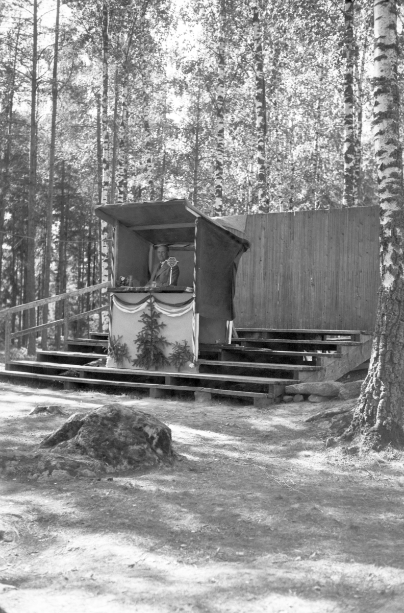 Håkon Prestkværn, Molunden i Moelv. Pyntet talerstol og taler, ukjent. 17. mai tale. Talerstolen i Molunden med trappeoppbygg for sangere og musikkorps. Mikrofon ved siden av taleren, ca. 1935-1939