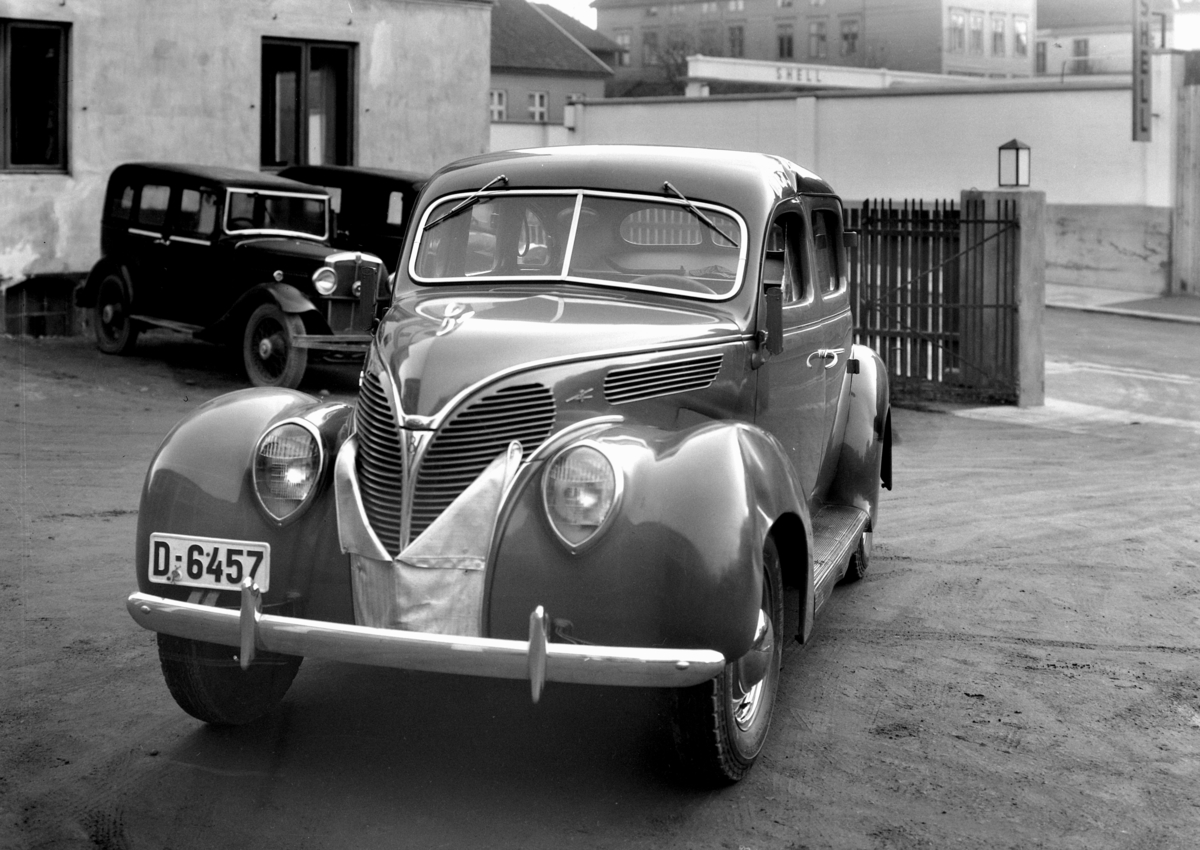 Normann Fotoatelier, Oplandske Auto. Ford V8 de luxe 1938. Kolisjonskadet personbil, D-6457. Hamar. I bakgrunnen trolig engelsk bil ca. 1933-35.