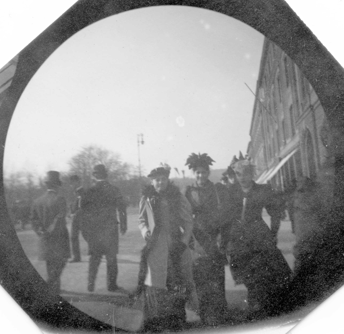 Fredrik Carl Mülertz Størmer, Tre damer, Frk. Bull i midten, spaserer langs Karl Johans gate, Oslo. To menn med ryggen til.