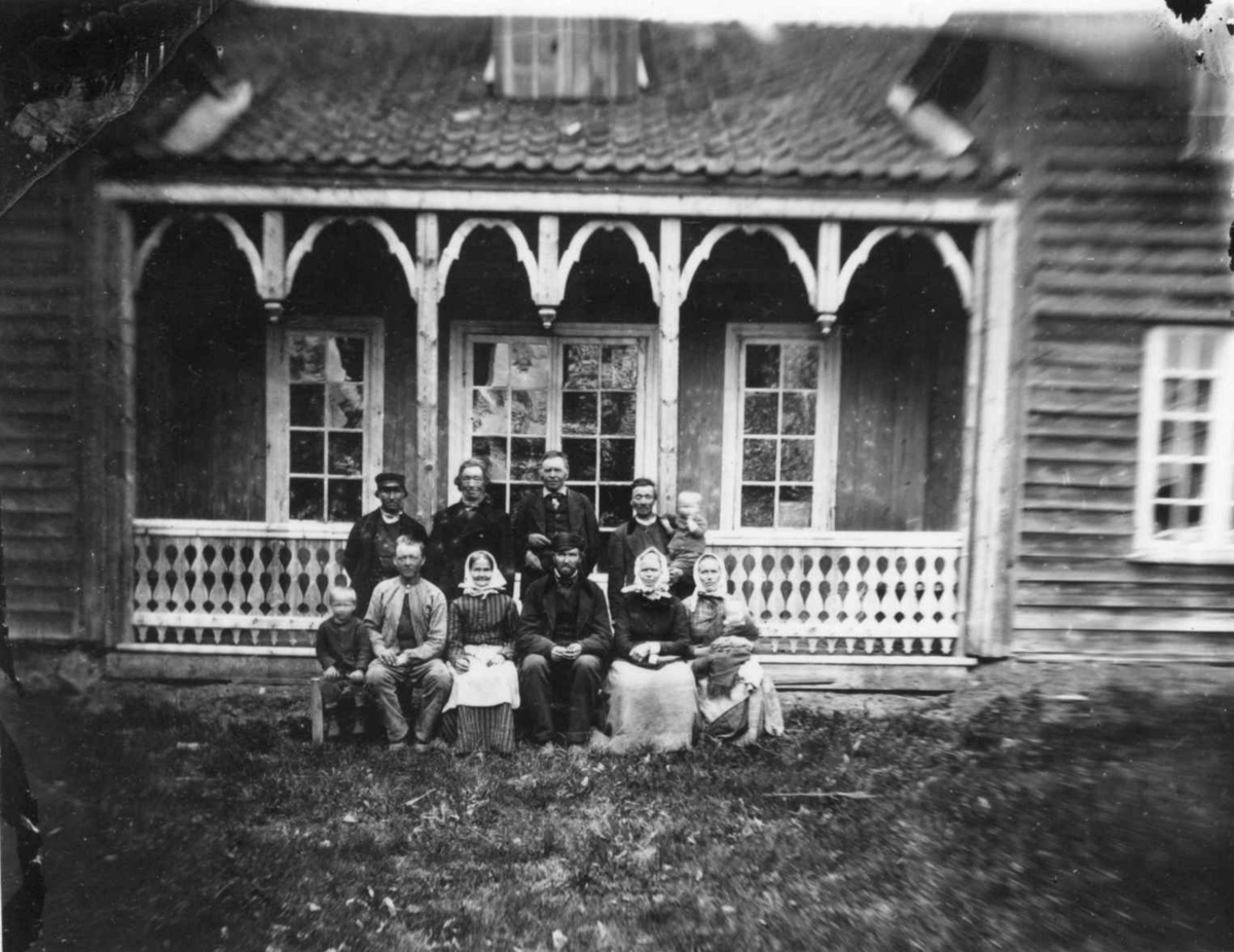 Fredrik Emil Faye, Husmannsfolk (ant.), Ullensaker. Gruppe barn og voksne poserer foran trebygning med søylerekke. Fra portrettserie av personer som bodde på eller besøkte Dal gård, Ullensaker, fotografert av gårdens eier, kammerherre Fredrik Emil Faye (1844-1903) i årene 1875-1900.