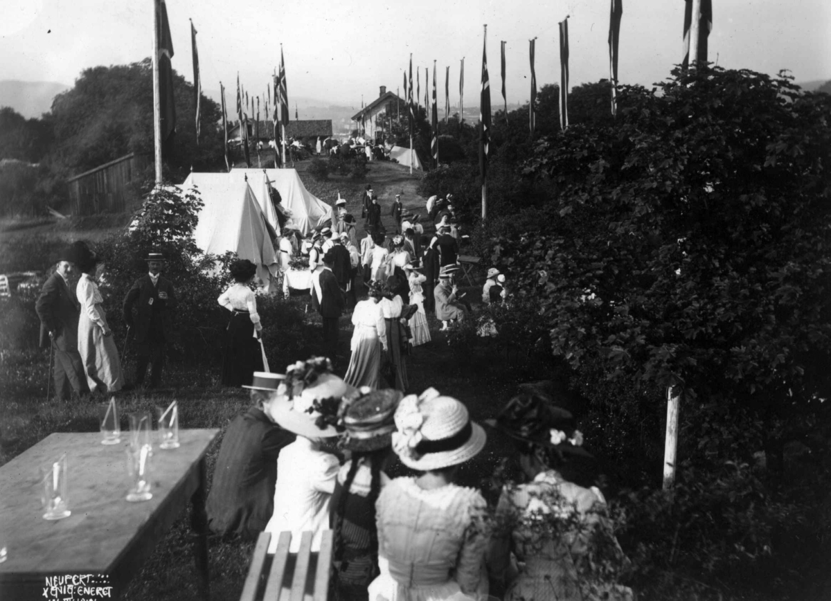 Hermann Christian Neupert, Hovedøya, Oslo. 1910. Sommermotiv. Fest. Kvinner og menn festkledd. Telt. Flagg. Bebyggelse.