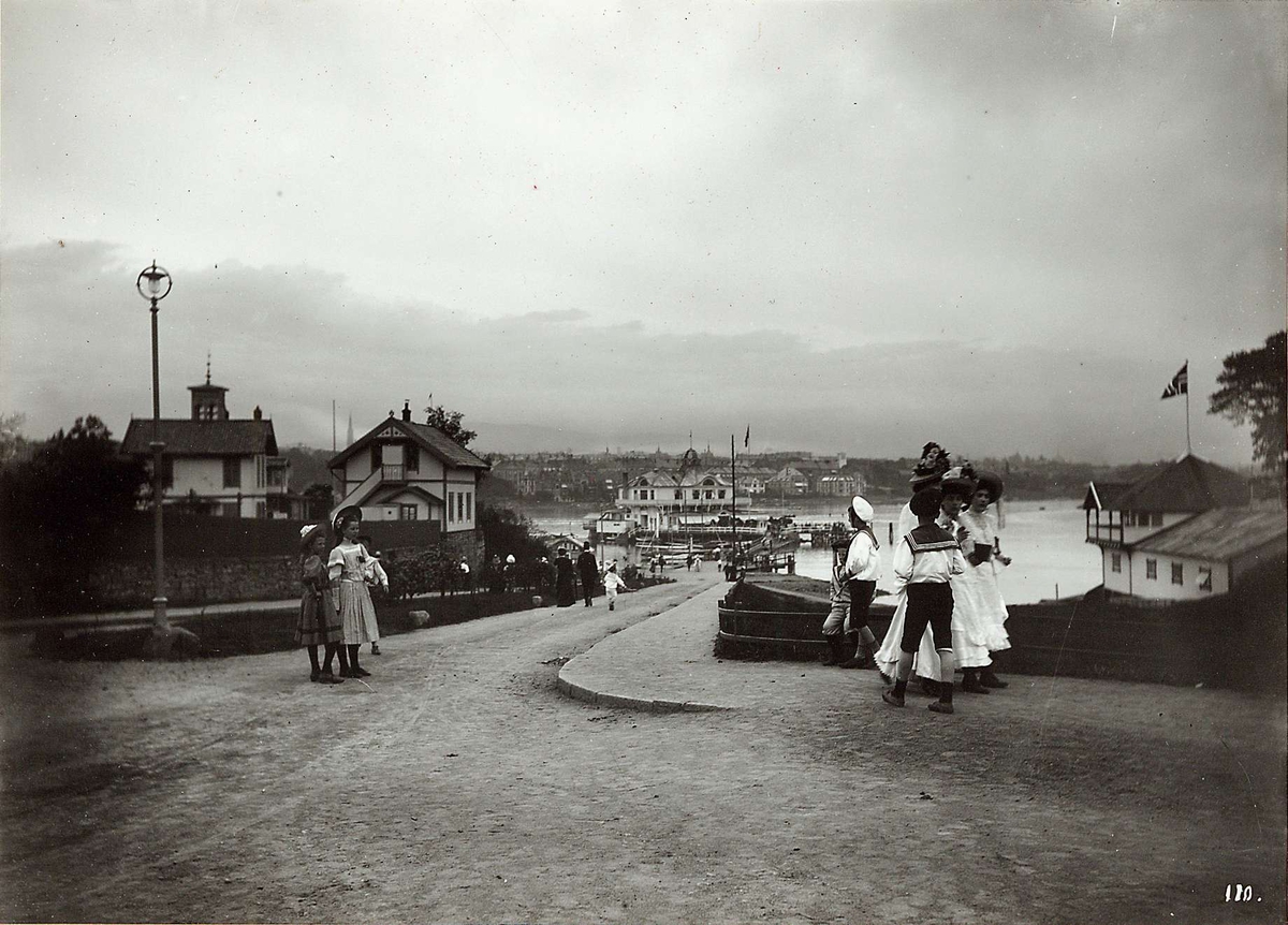 Hermann Christian Neupert, Dronningen, Bygdøy, Oslo 1908. Mennesker på veien mot Dronningen. Gutter i matrosdrakt. Unge kvinner i lange og med hatter.