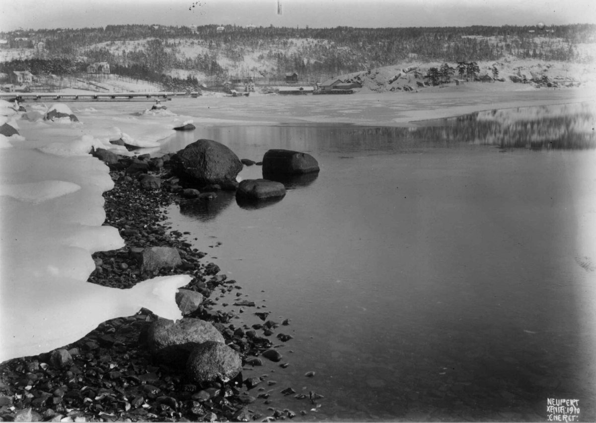 Hermann Christian Neupert, Oslo, Ormøya 1910. Oversiktsbilde. Strandparti. Vinter med is. Bebyggelse. Bro.