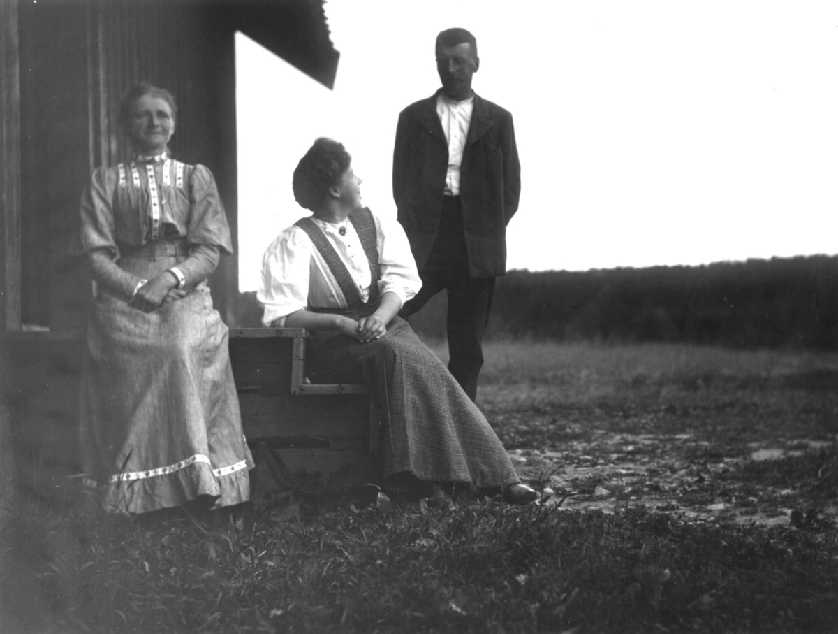 Hermann Christian Neupert, Bærum, Akershus 1908-1910. Landskap. I frogrunnen to kvinner og en mann foran et hus.
